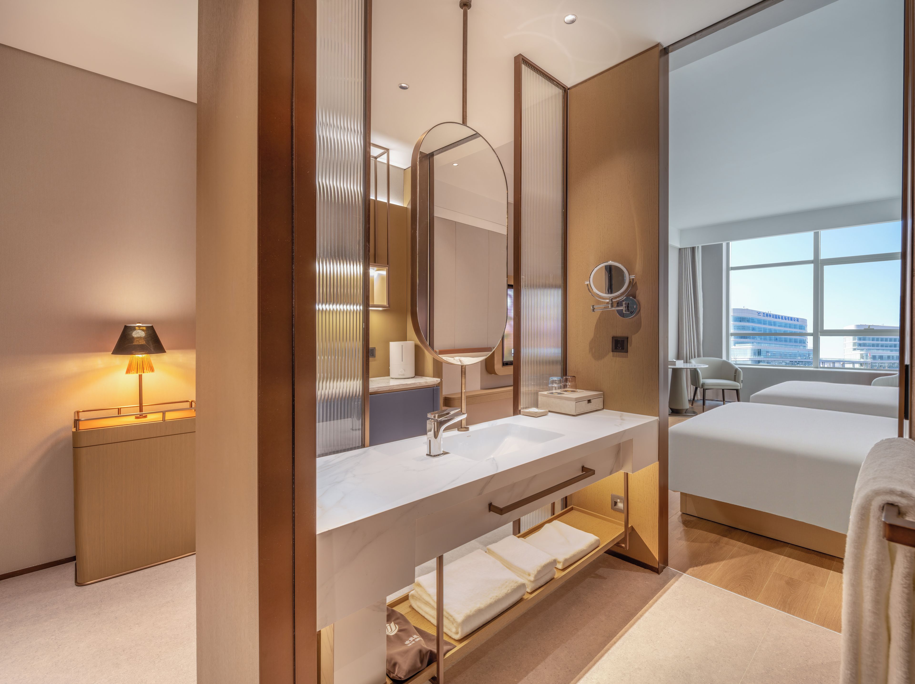 A modern hotel room with a large bed, a bathroom with a vanity, a mirror, and a view of the city.