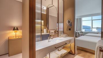 A modern hotel room with a large bed, a bathroom with a vanity, a mirror, and a view of the city.