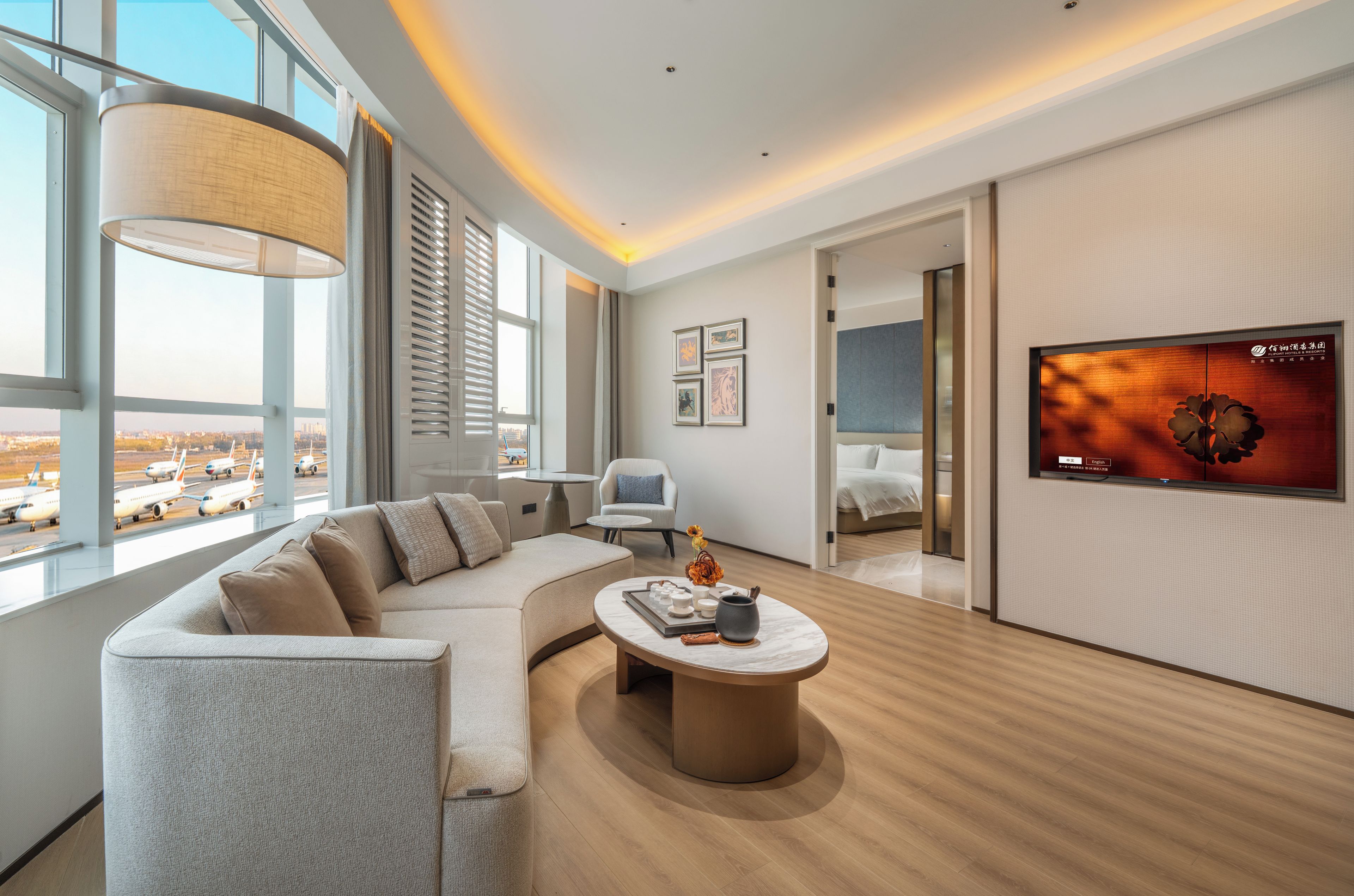 Ein modernes Hotelzimmer mit einer gebogenen Couch, einem runden Couchtisch und einem an der Wand befestigten Fernseher.