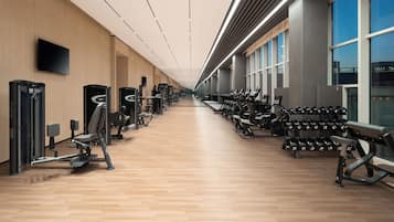 Ein Fitnessraum mit Trainingsgeräten, Holzboden und großen Fenstern.