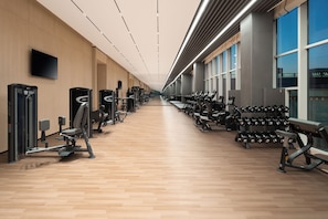 Un gimnasio con equipamiento de ejercicio, suelo de madera y ventanas amplias.