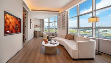 A modern living room with a large window, a sofa, a coffee table, and a TV mounted on the wall.