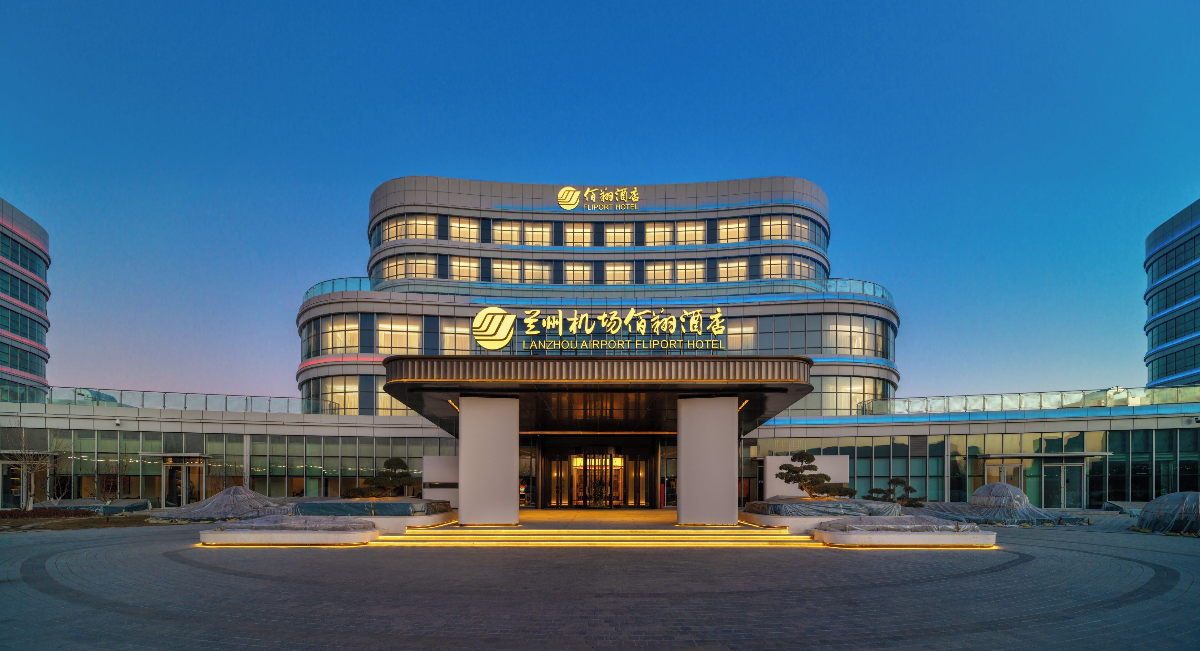 A modern hotel with a curved facade, illuminated signage, and a spacious entrance area.