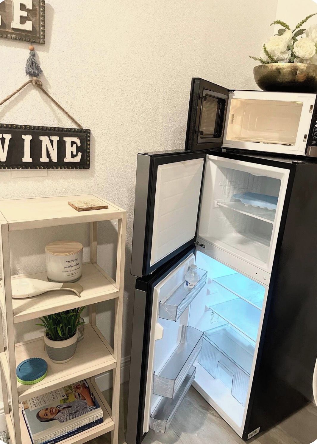 Una cocina con refrigerador, microondas y repisa con una vela y un libro.