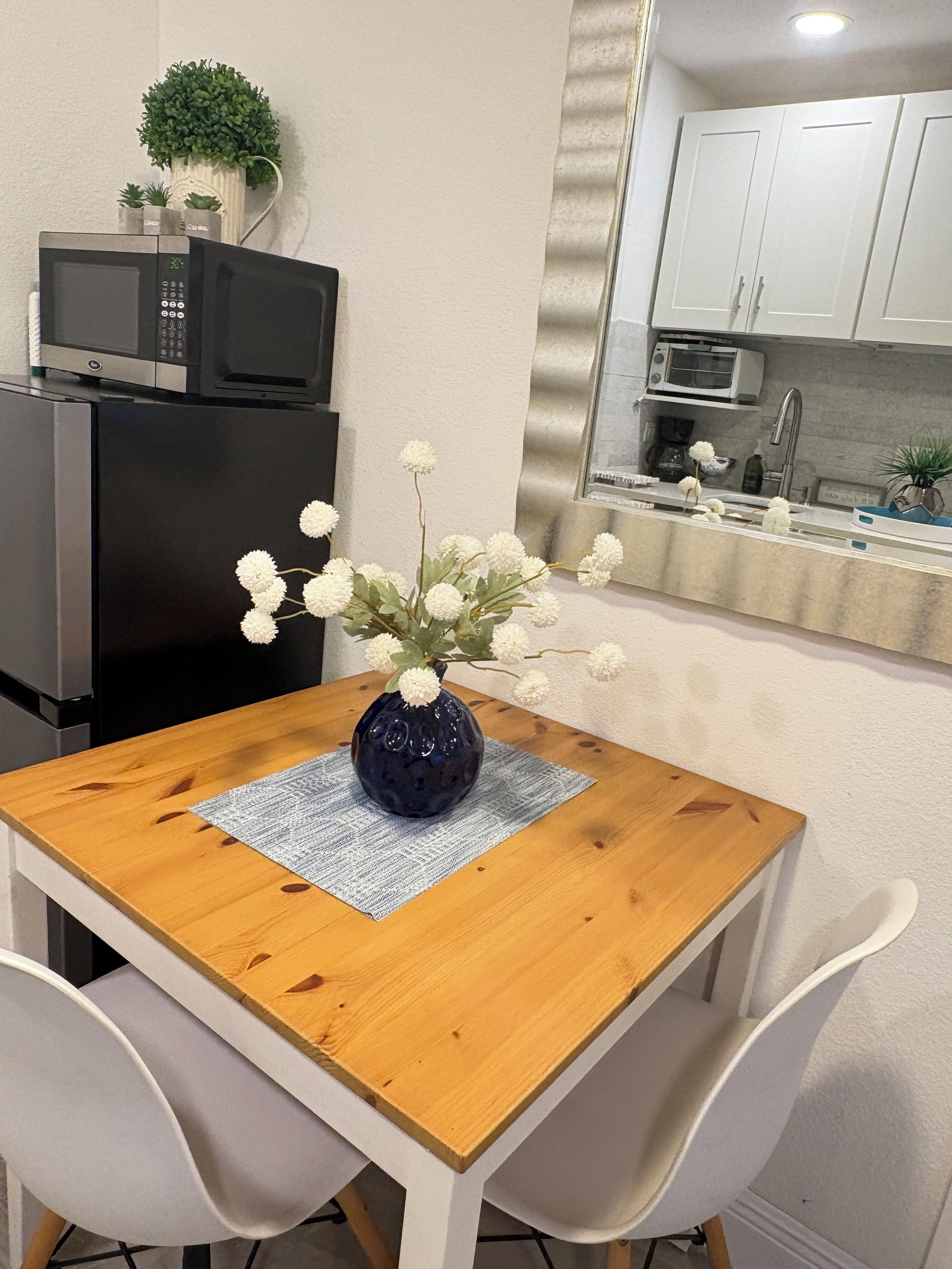 Un coin repas avec une table en bois, des chaises blanches et un vase bleu contenant des fleurs blanches.