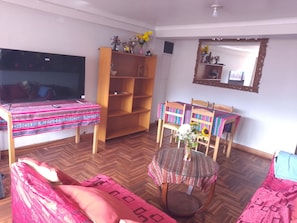 A room with a bed, a wooden bookshelf, a dining table with chairs, a round glass table, and a mirror on the wall. - The Awakening of the Inca (Cusco)