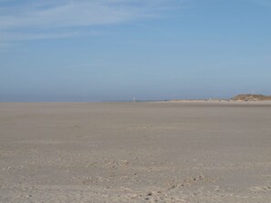 Een breed, vlak strand met een verafgelegen vuurtoren.