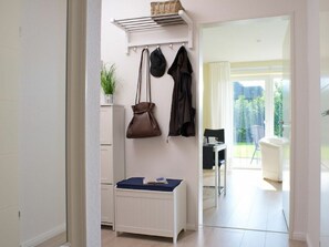 Een kamer met een witte kast, een klein tafeltje met een blauwe tafelkleed, een kapstok met een bruine tas en een zwart jasje, en uitzicht op een balkon met een stoel en een tafel.