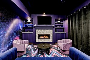A room with a fireplace, two armchairs, a coffee table, and a wall with a space-themed mural.