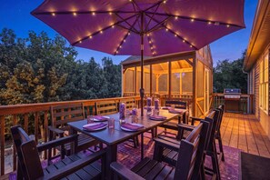 Un espace de restauration en plein air avec une table dressée pour quatre personnes, entourée de chaises en bois et d’un grand parasol violet.