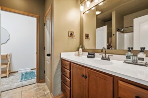 Une salle de bain avec un double lavabo, un meuble-lavabo et un grand miroir. On y trouve deux flacons de savon liquide et de lotion sur le lavabo.