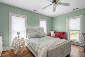 A bedroom with a bed, a nightstand, a red chair, and a window with blinds. - Charming 3-bedroom house near KC that sleeps up to 8 with gazebo and coffee bar. (Olathe)