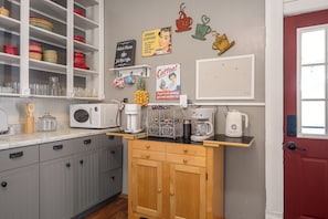 A kitchen with a microwave, coffee maker, and a coffee station. There are shelves with dishes and a refrigerator. - Charming 3-bedroom house near KC that sleeps up to 8 with gazebo and coffee bar. (Olathe)