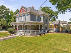 A two-story house with a porch, a chimney, and a well-maintained lawn. - Charming 3-bedroom house near KC that sleeps up to 8 with gazebo and coffee bar. (Olathe)