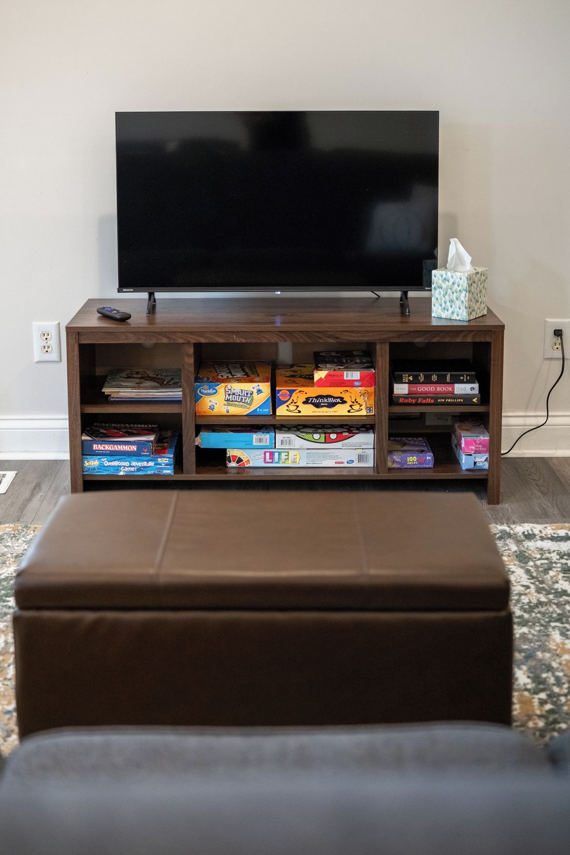 A living room with a flat-screen TV on a wooden stand, a remote control, and a tissue box on the stand.