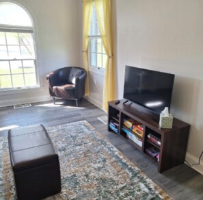 A living room with a television, a leather chair, a rug, and a window with curtains. - Country Quiet, Town Close - Charming Cleveland Cottage Near OCI & More (Cleveland)