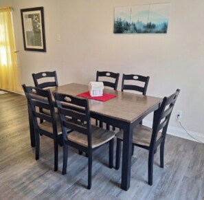 A dining area with a rectangular table surrounded by four chairs, a red placemat, and a white object on the table. - Country Quiet, Town Close - Charming Cleveland Cottage Near OCI & More (Cleveland)