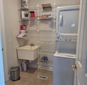 A laundry room with a washing machine, a sink, and shelves with various items.
