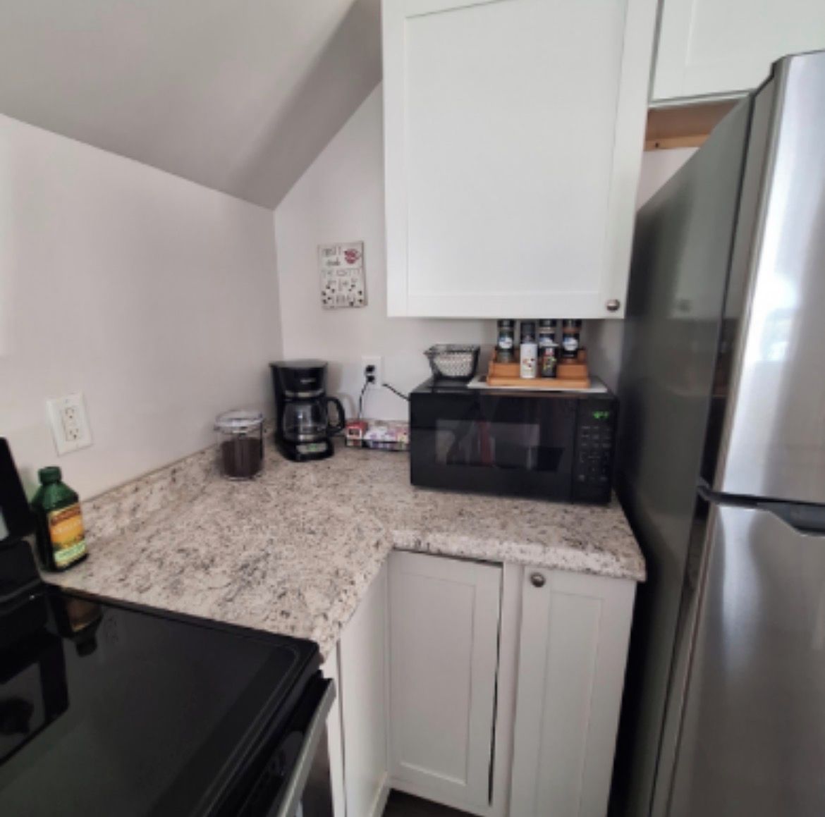 A compact kitchen with a microwave, coffee maker, and a stainless steel refrigerator.