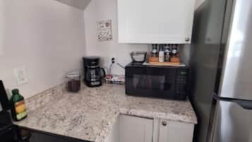 A compact kitchen with a microwave, coffee maker, and a stainless steel refrigerator.