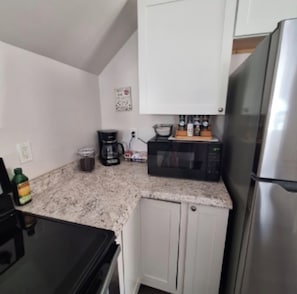 A compact kitchen with a microwave, coffee maker, and a stainless steel refrigerator.
