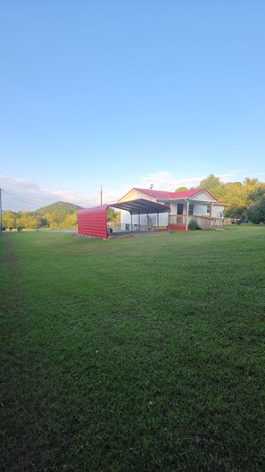 A large open grassy field with a red metal structure and a white building with a red roof.
