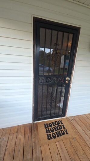A black metal door with decorative elements, a wooden deck, and a doormat with text.