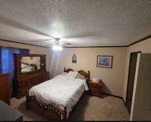 A bedroom with a bed, dresser, mirror, ceiling fan, and a framed picture on the wall.