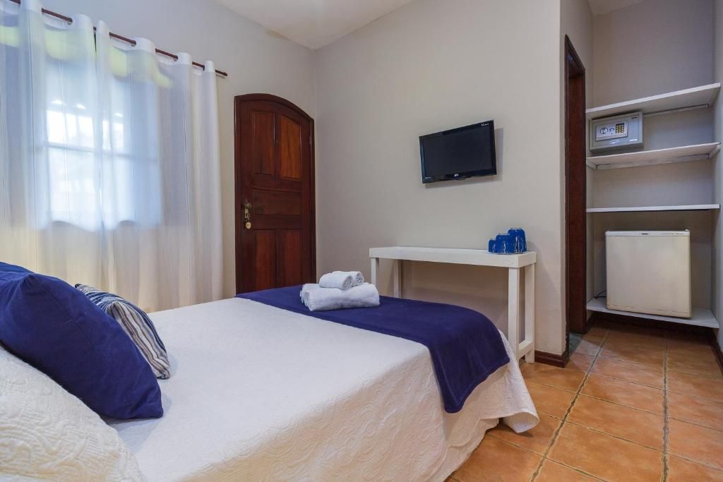 Een hotelkamer met een bed, een televisie, een klein tafeltje met kopjes en een minibar.