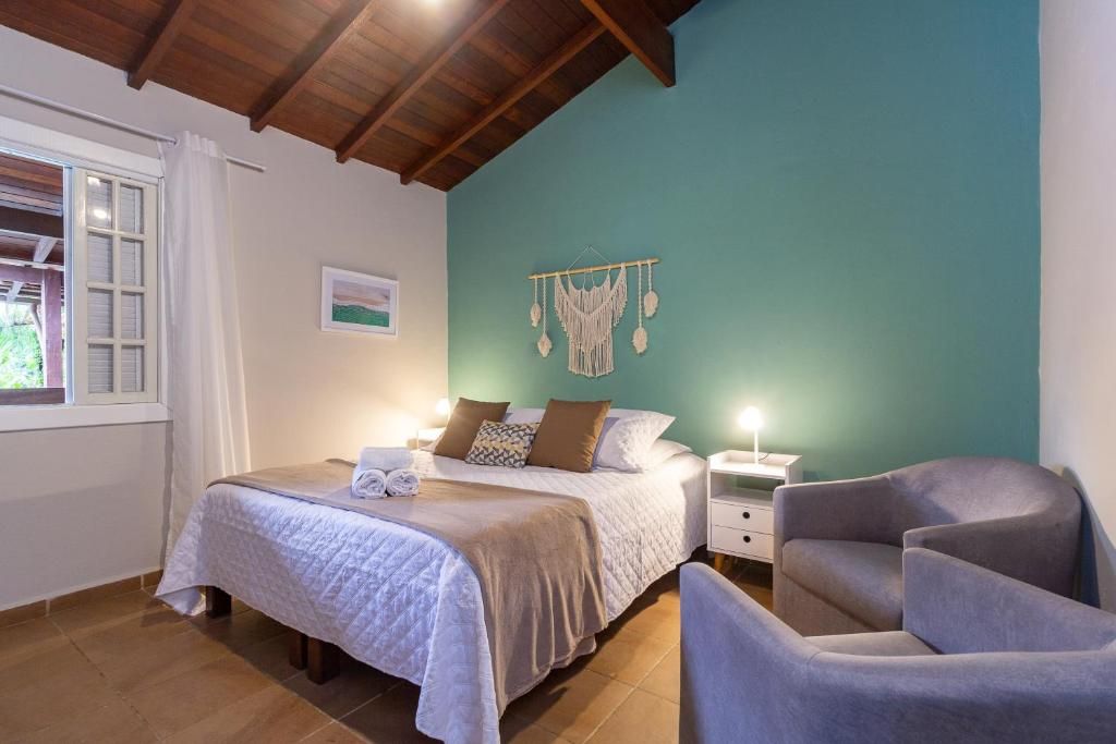 Een slaapkamer met een bed, nachtkastjes, een stoel, een wanddecoratie en een raam met gordijnen.