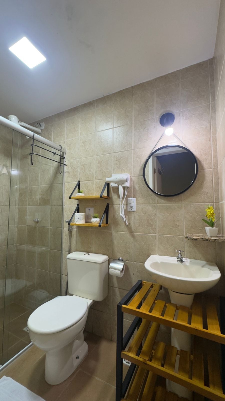 Een badkamer met toilet, wastafel en douche. Boven de wastafel hangt een spiegel en aan het plafond een lamp.