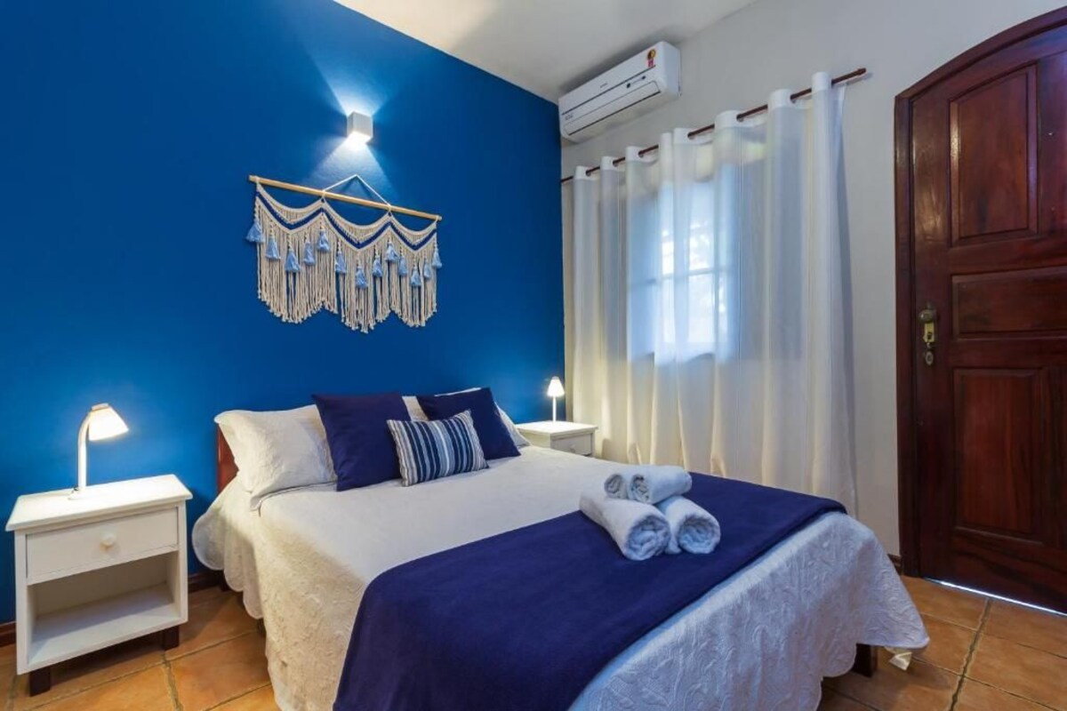 Une chambre d’hôtel avec un lit, une table de chevet, un climatiseur fixé au mur, une porte en bois et un rideau.