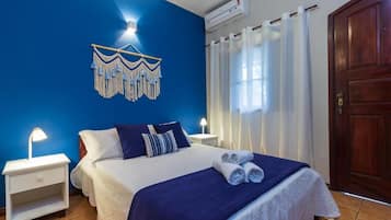 Una habitación de hotel con una cama, una mesita de noche, un aire acondicionado de pared, una puerta de madera y una cortina.