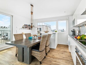 A modern kitchen with a dining area, featuring a large table, wicker chairs, and a view of the city. - Houseboat in Olpenitz With Swimming Pool (Kappeln)