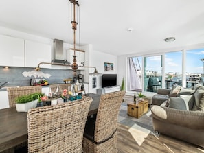 Un espacio moderno con zona de comedor, cocina y un amplio ventanal con vistas a un puerto deportivo.