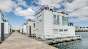 A waterfront property with a wooden dock leading to a white building with multiple windows and balconies. - Houseboat in Olpenitz With Swimming Pool (Kappeln)