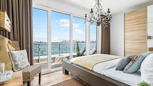 A bedroom with a large window, a bed, a chandelier, and a view of the water. - Houseboat in Olpenitz With Swimming Pool (Kappeln)