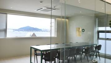 Ein Konferenzraum mit Glastisch und Stühlen, Blick auf eine Brücke und Berge durch das Fenster sowie ein 'Voda Stay'-Logo an der Wand.