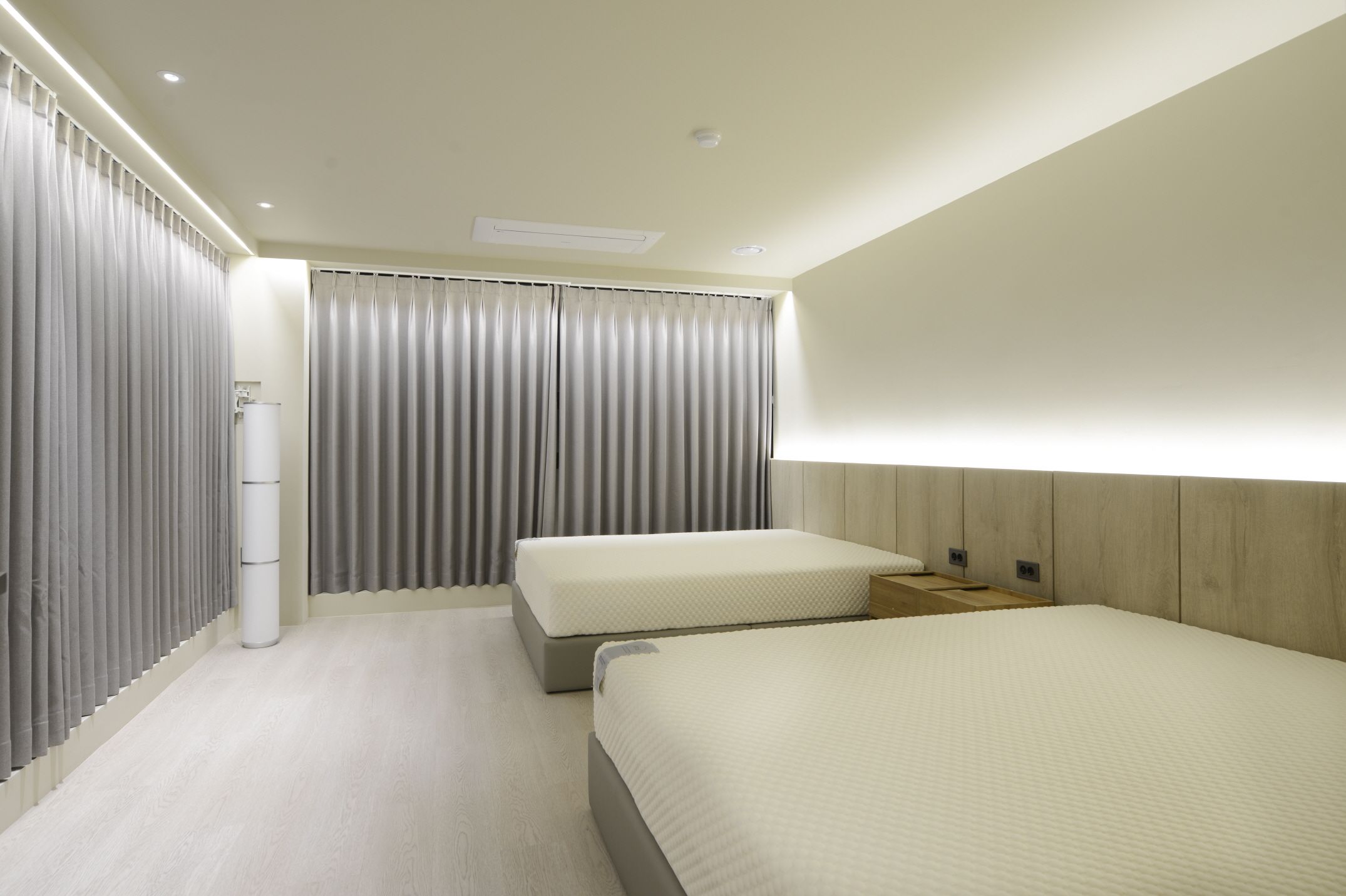 Ein Hotelzimmer mit zwei Betten, einem großen Fenster mit Vorhängen, einem Holz-Kopfteil und einer weißen Wand.