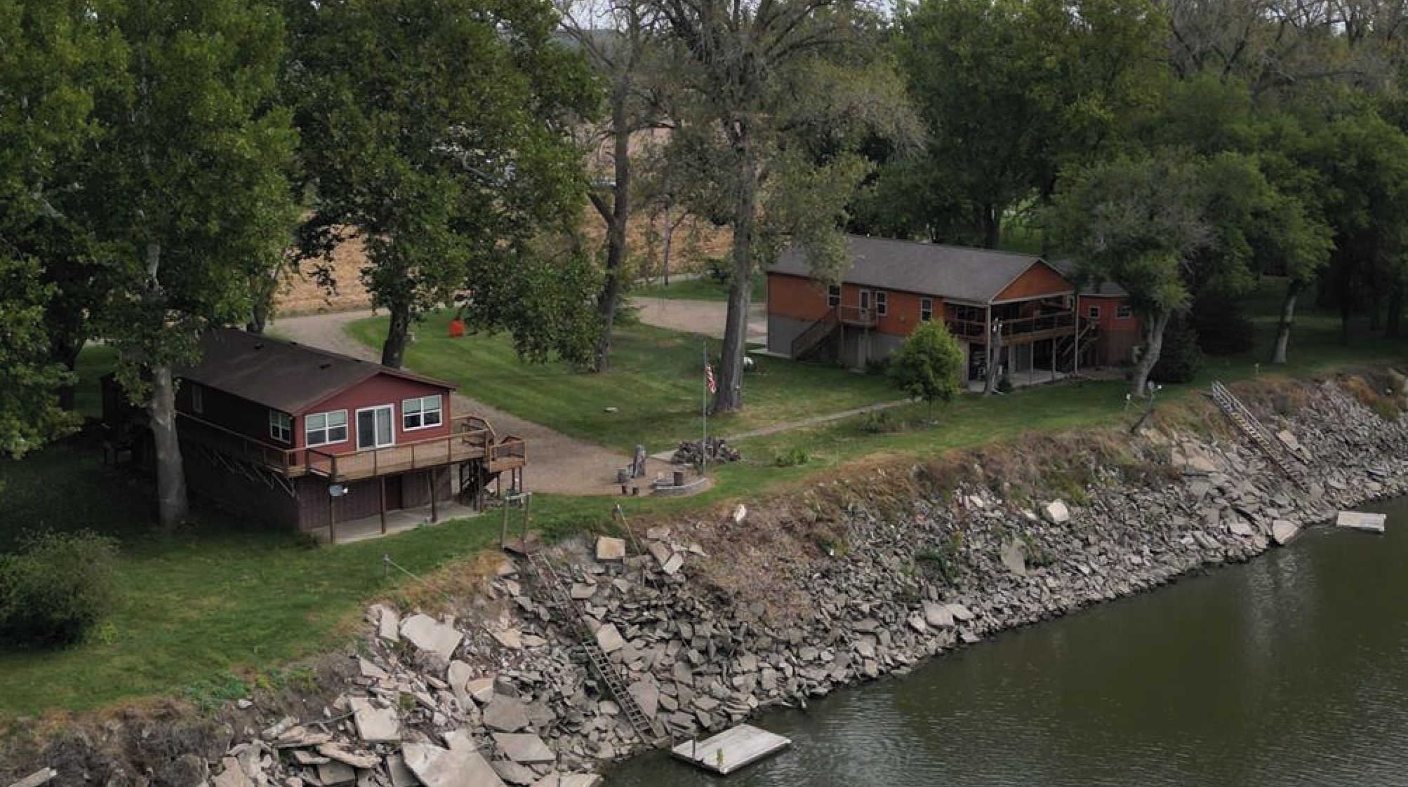 A lakeside property with two main buildings, a dock, and a rocky shoreline.