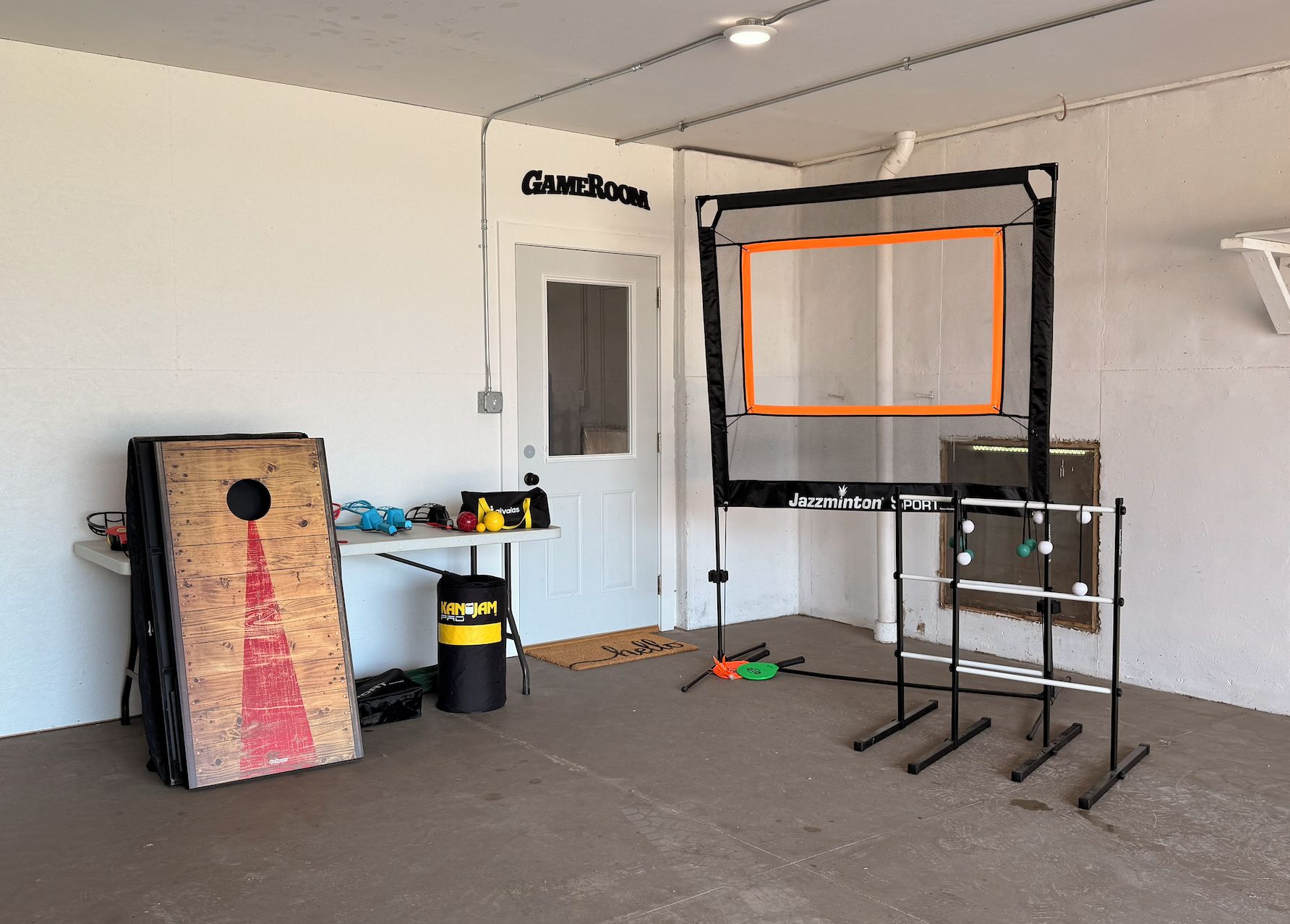 Un garaje con un trampolín, una puerta que dice 'Gameroom' y un estante con equipo deportivo.