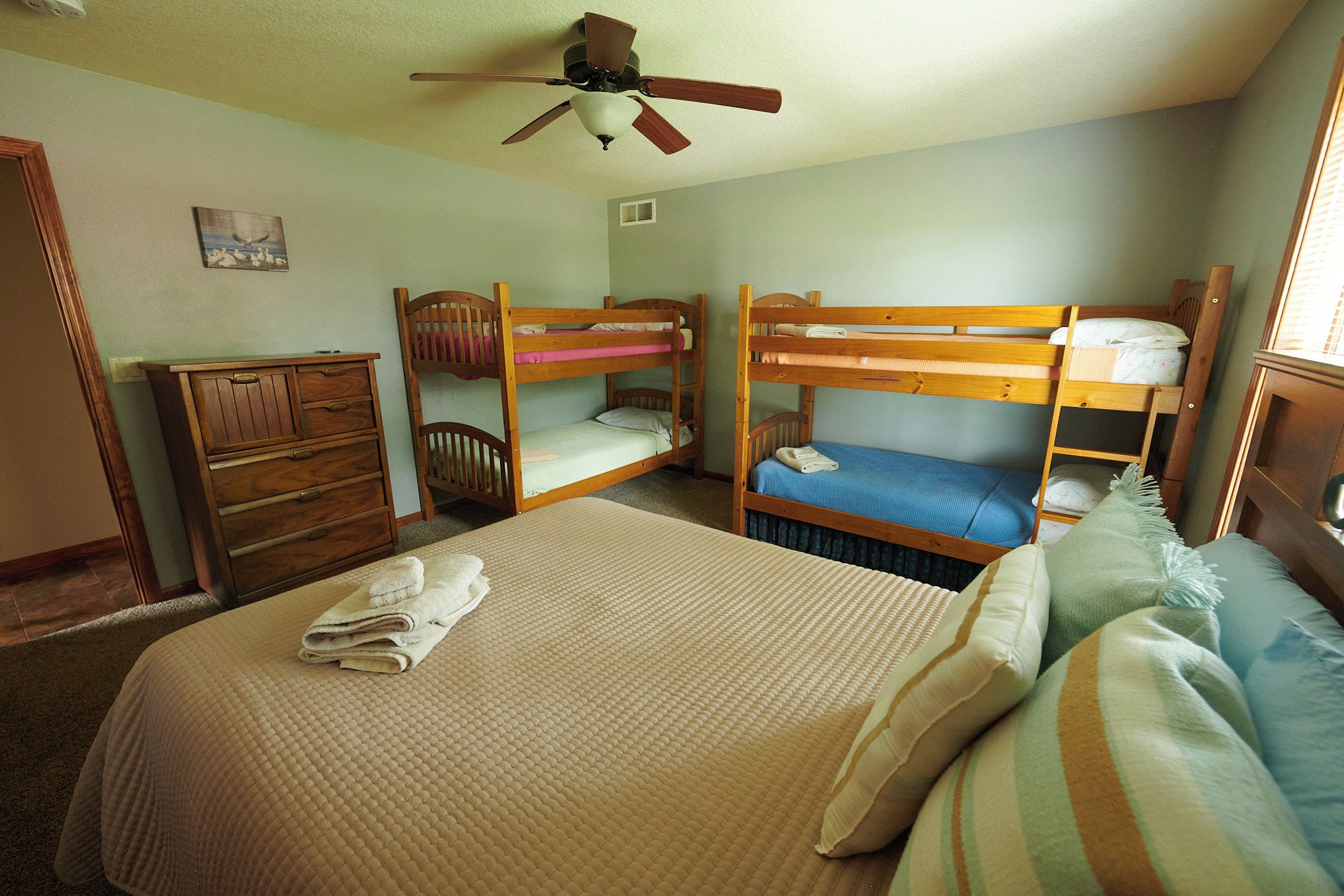 Un dormitorio con literas, ventilador de techo, cómoda y cama con cubrecama acolchado.