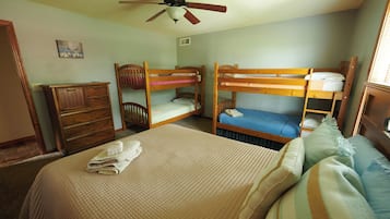 Un dormitorio con literas, ventilador de techo, cómoda y cama con cubrecama acolchado.
