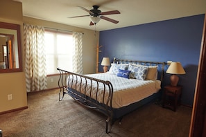 A bedroom with a bed, two bedside lamps, a ceiling fan, and a window with curtains.