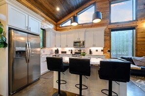 A modern kitchen with white cabinets, stainless steel appliances, and a bar area with stools. - Luna Wolf Lodge · New Listing! Hot Tub, Fire Pit & Loft Bunks in the Pines (Broken Bow)