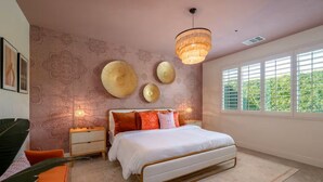Een slaapkamer met een bed, nachtkastjes, een hanglamp en een raam met luxaflex.
