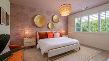 A bedroom with a bed, bedside tables, a hanging light fixture, and a window with blinds.