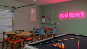 A pool table with billiard balls, a neon sign reading 'DESERT DREAMING,' and a dining area with chairs and a table.