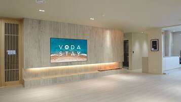 Eine moderne Hotelhalle mit einem großen, an der Wand befestigten Fernseher, der 'VODA STAY' anzeigt, und einem Empfangstresen.