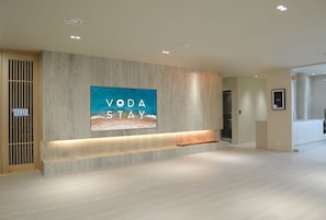 Eine moderne Hotelhalle mit einem großen, an der Wand befestigten Fernseher, der 'VODA STAY' anzeigt, und einem Empfangstresen.